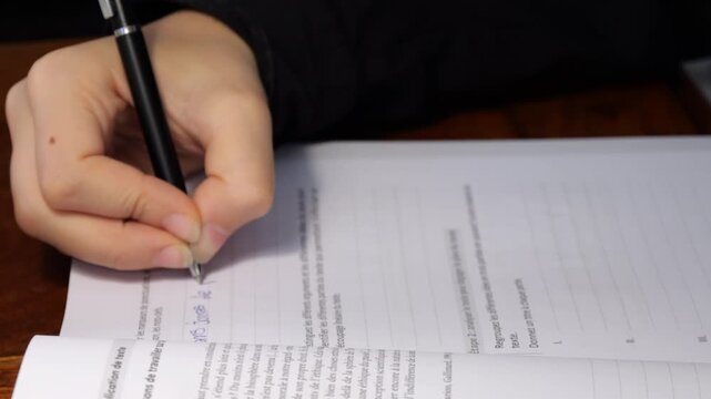 50p insert shot of a student's hand writing notes in a workbook during a study session, highlighting learning, education and academic preparation