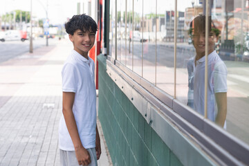 Handsome teenage boy shopping on a commercial street, with the reflection of a shop or entertainment venue visible. © Inspiraciones