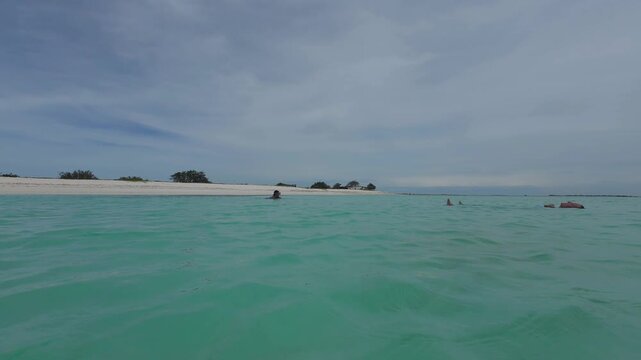 Refreshing POV view of a relaxing tropical getaway, capturing the serene beauty of calm sea waves and bright white sandbars under a soft cloudy sky.