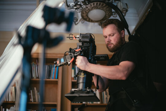 The director of photography with a camera on the set. A professional videographer is working on filming a movie or commercial for a TV series. The filming process takes place indoors in a studio.