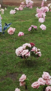 Vertical video. Rain falling on wedding flowers arranged on green grass in a forest clearing.