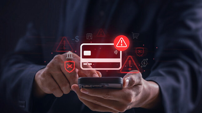 Close up of hands holding a smartphone with glowing red credit card icon and warning alert symbols depicting online financial fraud or cyber security breach