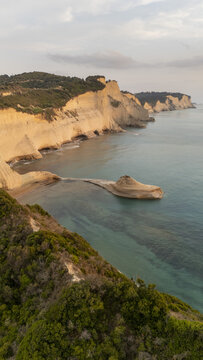 Aerial view of Cape Drastis featuring dramatic limestone cliffs, turquoise waters, and lush green vegetation along the coastline in Corfu, Greece.