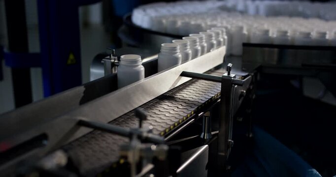 High angle view of white plastic bottles being single indexed from rotating table onto straight conveyor belt