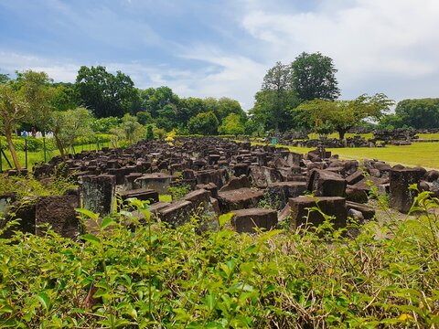 Trowulan archaeological site boasts ancient stone ruins amidst lush green trees under a sunny blue sky  ideal travel brochure imagery.