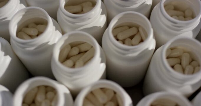 Top view close up of numerous open white plastic bottles filled with medical capsules on production line