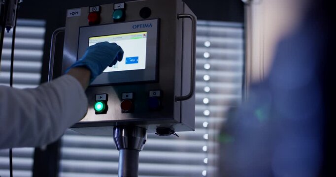 Close up of operator wearing blue glove pressing buttons and using touchscreen on industrial control panel