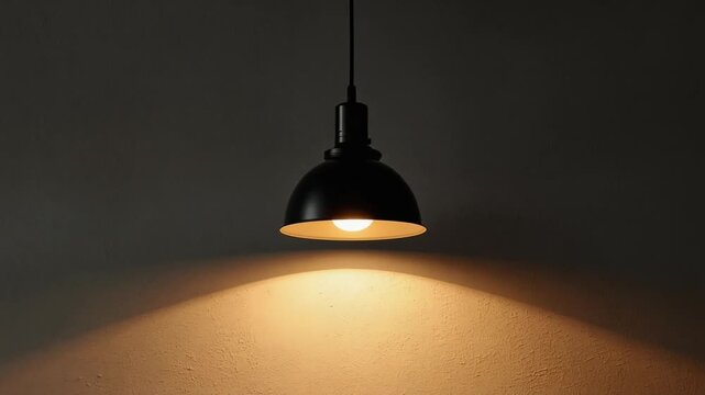 Black industrial pendant lamp illuminates a textured surface with warm glowing light in this high resolution motion video clip
