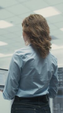 360 Degree Vertical Screen. Caucasian Woman It Specialist Holds Laptop Computer in Modern Data Center, Inspecting Server Racks, Analyzing Network Data, and Managing Cloud Infrastructure. Tracking Shot