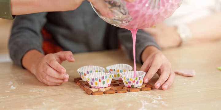 Cropped hands pouring pink batter into cupcake liners for baking