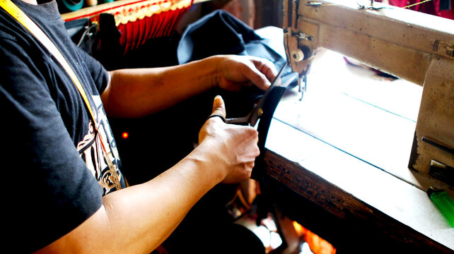 Close-up of a tailor cutting black fabric with scissors next to a sewing machine