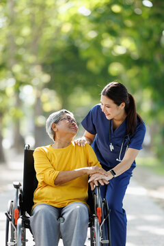 Caregiver assisting senior woman in wheelchair outdoors, showing support, compassion, and shared happiness during an assisted living or home care walk in nature