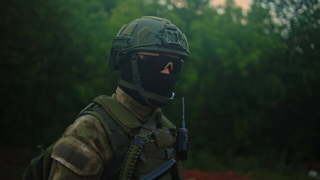 Soldier in tactical gear turning head and torso while holding radio in woodland, side view with soft natural light, camouflage uniform, helmet, and muted forest backdrop