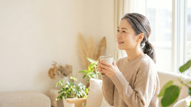Sunlit mature woman holding warm coffee mug in cozy living room smiling toward peaceful contentment perfect for lifestyle advertising and wellness presentation