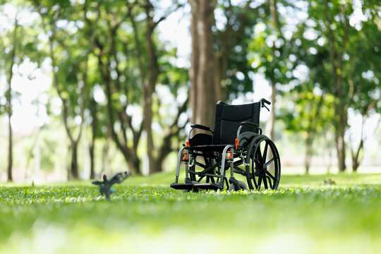 Empty wheelchair resting in a lush green park during daytime, representing concepts of disability, health, recovery, mobility aid, nature, rehabilitation, and loneliness outdoors