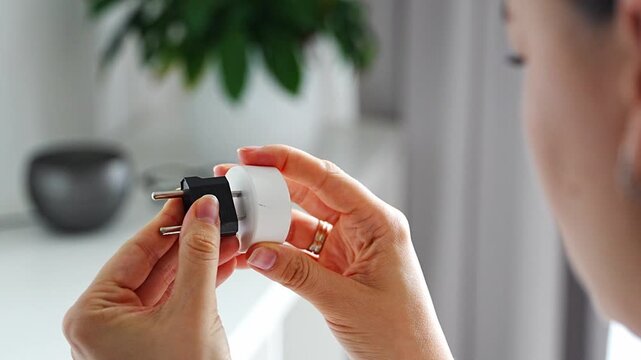Woman compares electrical plug adapters for different power outlets at home. International travel and power compatibility concept for global electronics.