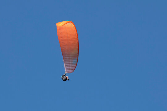 Vol en parapente dans un ciel bleu azur d'&eacute;t&eacute; en montagne. Voile orange.