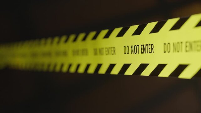 A "Do Not Enter" tape barrier is visible, illuminated by police vehicle lights; the area is hazardous and designated as a restricted crime scene. Shot using a tilt-shift lens.