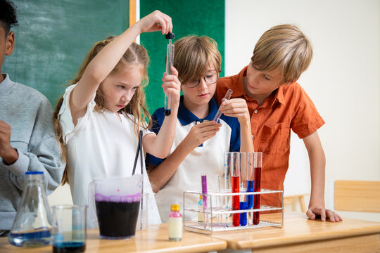 Diverse elementary school children using droppers and test tubes during a chemistry science experiment in classroom. Students collaborating on scientific laboratory project with colorful liquids.