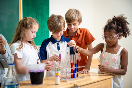 Diverse elementary school children using droppers and test tubes during a chemistry science experiment in classroom. Students collaborating on scientific laboratory project with colorful liquids.