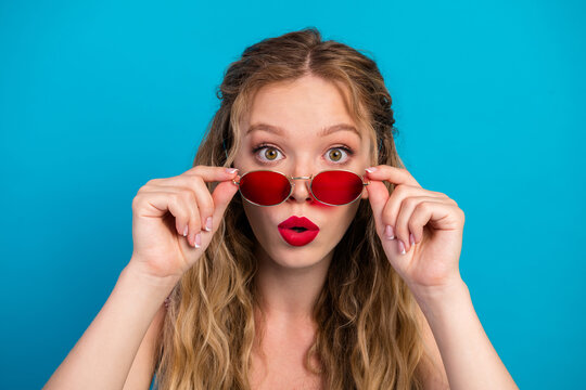 Glamorous young woman with red sunglass peeking over stylish frame against blue background for fashion lifestyle and advertising