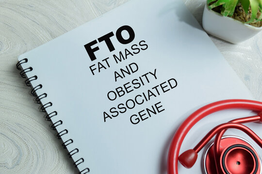 Concept of FTO - Fat Mass and Obesity Associated Gene research write on book isolated on Wooden Table. For genetic predisposition to obesity and DNA variants