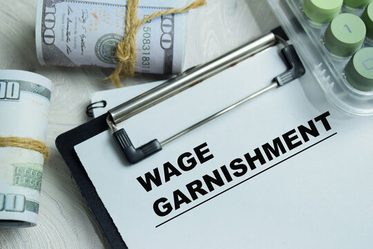 Concept of wage garnishment write on clipboard isolated on Wooden Table. For debt collection process and employee income withholding