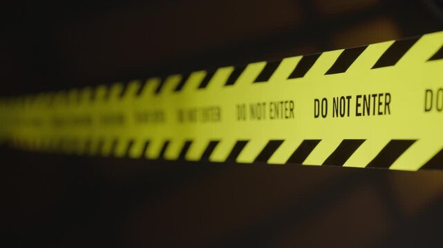 The shot shifts focus from the background to the foreground, revealing a "Do Not Enter" barrier tape illuminated by police lights; it is a restricted danger zone an active crime scene.