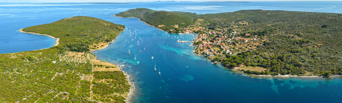 Panorama of village of Ilovik, Croatia, with traditional red-roof houses surrounded by olive groves and dry stone walls. The narrow channel is filled with white sailboats