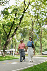 Fototapeta premium Mother and daughter are walking hand in hand. Smiling and sharing a strong generational bond. Enjoying retirement and a healthy lifestyle together in a green park environment