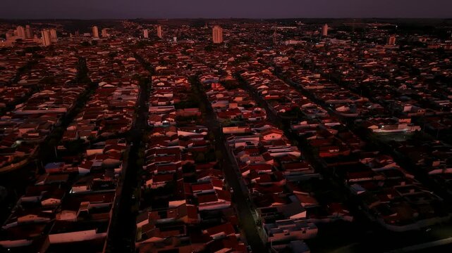 Aerial view of a residential neighborhood at dusk with rows of houses and distant city buildings