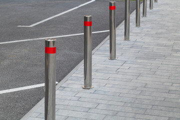 Row of modern stainless steel bollards with bright red reflective bands installed along a paved sidewalk to enhance pedestrian safety and restrict vehicle access. © Tanya