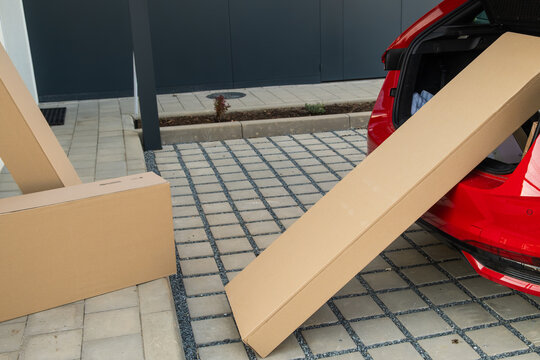 Unloading cardboard boxes from vehicles trunk onto outdoor paved surface. Two large parcels positioned at a slight angle on the ground, ready for transport.