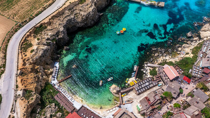 aerial drone view of anchor bay on south malta coast with crystal clear Mediterranean Sea water and boats with cliffs surrounding in summer © STJMEDIA