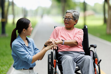 Obraz premium Caregiver providing emotional support and assistance to senior woman sitting in a wheelchair, holding her hand while conversing in a natural outdoor park setting