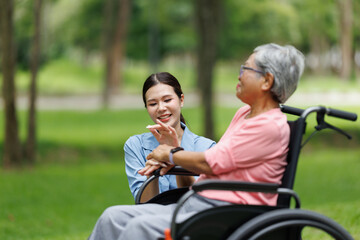 Obraz premium Asian caregiver providing support and companionship to an elderly woman in a wheelchair, enjoying a happy outdoor moment in a park, representing assisted living and compassionate nursing care
