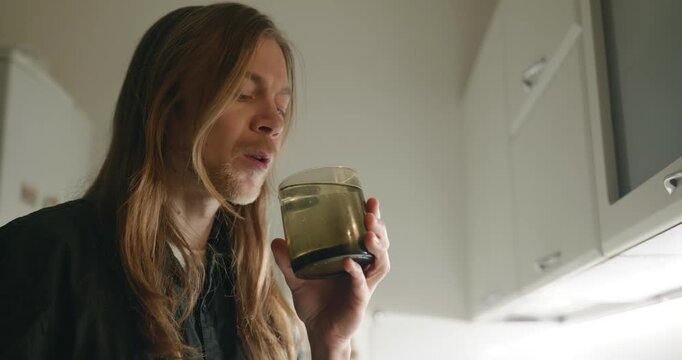 Caucasian man drink hot water in evening. Single male is drinking tea at kitchen at home. 4K 10-bit
