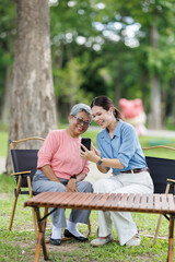 Fototapeta premium Granddaughter and grandmother sitting outdoors in a park, enjoying quality time together and sharing a happy moment while looking at a smartphone, bridging generations with technology