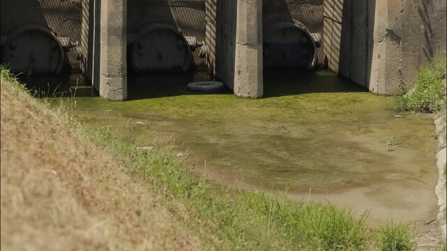 Closed water control gates at the canal connecting Jarun Lake and the Sava River with exposed mud and algae in Zagreb Croatia.