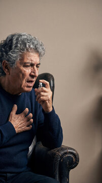 Senior man using nitroglycerin spray for angina pectoris relief. Elderly male patient experiencing cardiovascular distress and chest pain. Heart disease treatment and therapy.