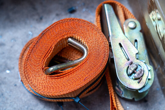 Top-down close-up of a coiled orange ratchet cargo strap with a metal mechanism.