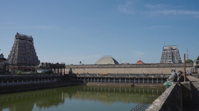 Wide shot of Chidambaram Nataraja Temple tank, Shivaganga theertham, towering gopurams and temple dome under blue sky. Dravidian architecture, Tamil Nadu, Hindu pilgrimage site, South India.