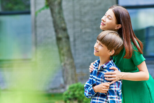 A loving mother embraces her joyful son in a lush garden.