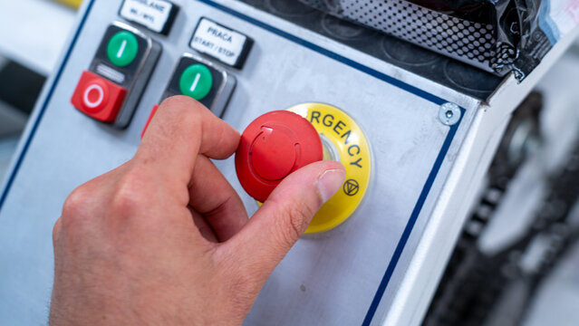 Worker pressing red emergency stop button on industrial machinery control panel