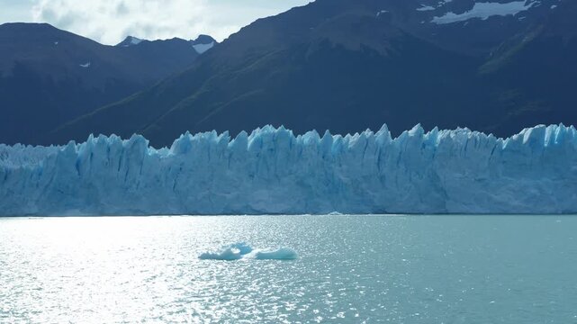Perito Moreno Glacier stretches across Argentino Lake in Los Glaciares National Park near El Calafate, Patagonia, Argentina, with floating ice and dark Andean slopes reflected on shimmering waters