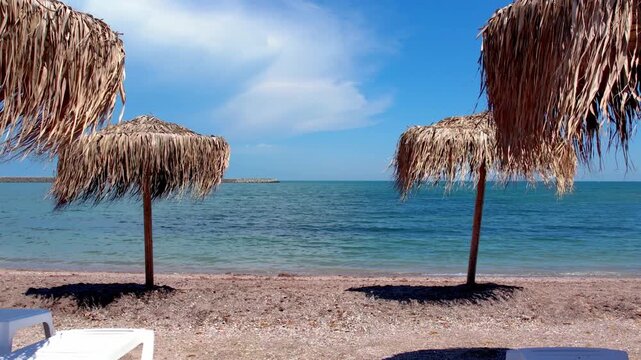 Thatched straw beach umbrellas framing a beautiful view of the calm blue sea on a sunny summer day. Slow motion video of beach umbrellas framing the calm turquoise ocean on a sunny summer day.