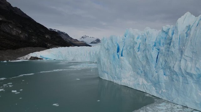 Perito Moreno Glacier rises above Argentino Lake in Los Glaciares National Park near El Calafate, Patagonia, Argentina, revealing towering blue formations beside floating fragments, drone forward fly