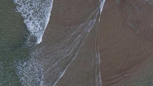 Aerial view of gentle ocean waves washing over sandy shore at Spanish Point Beach