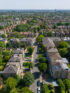 Aerial view of Ealing residential streets featuring rows of Victorian houses, lush green trees, and parked cars along the road in London Borough of Ealing, England, United Kingdom.