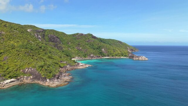 Aerial drone shot from Anse Major to Anse Du Riz in Mahe, Seychelles, revealing turquoise coastal waters, steep granite cliffs, and pristine tropical beaches